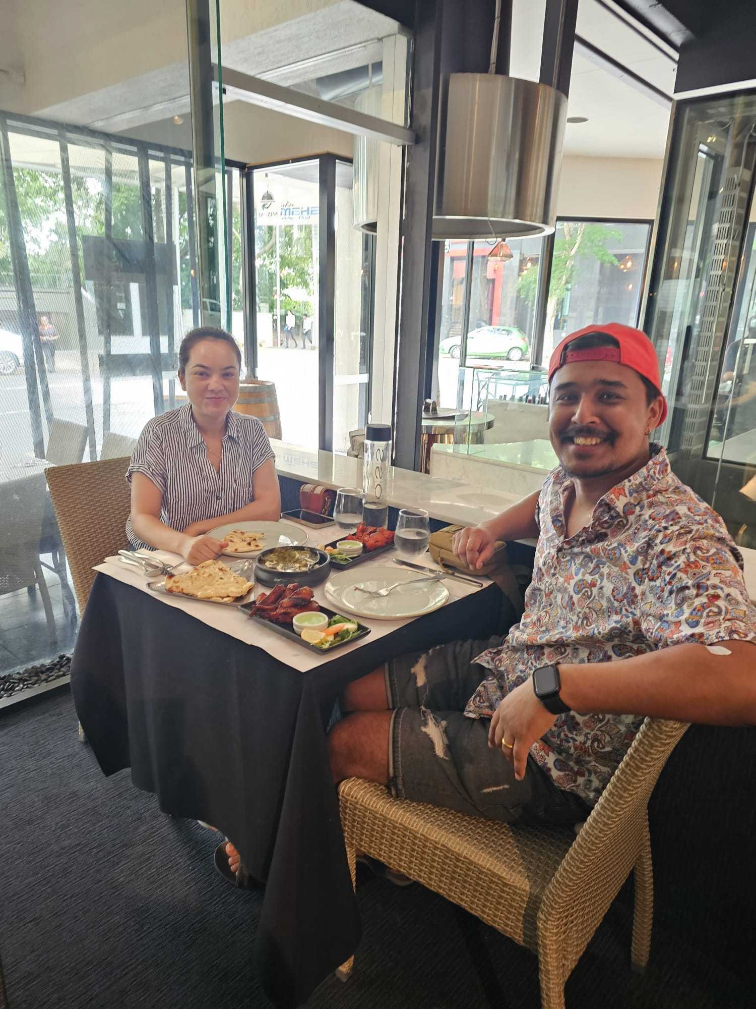 Two guests with naan, starters, and a curry at a window table