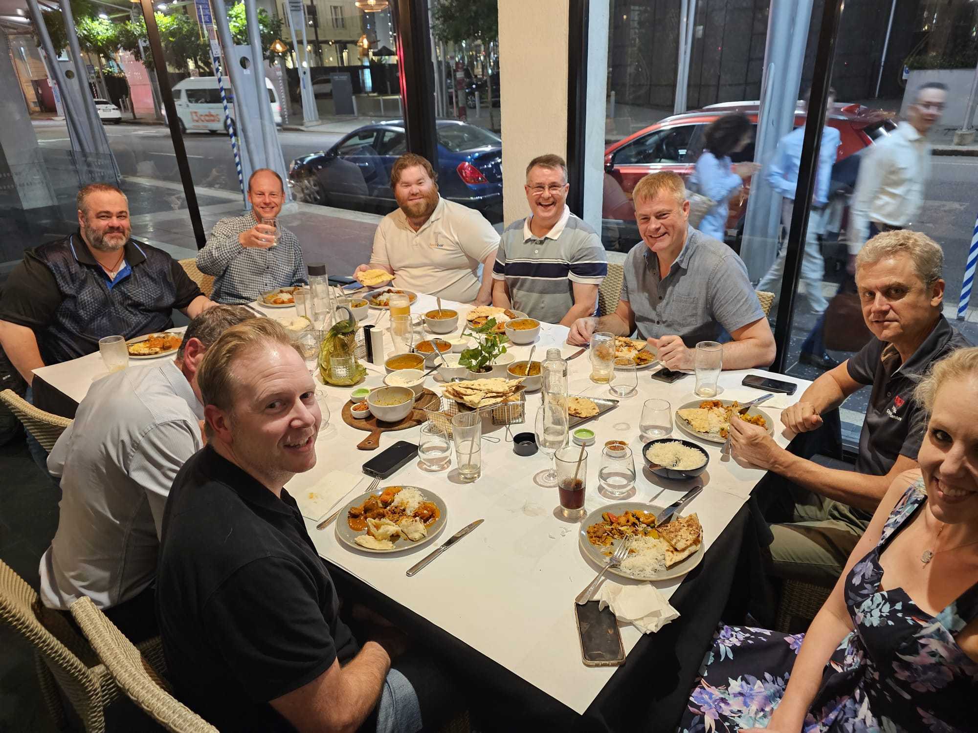 A large group sharing curries, rice, and bread by the windows