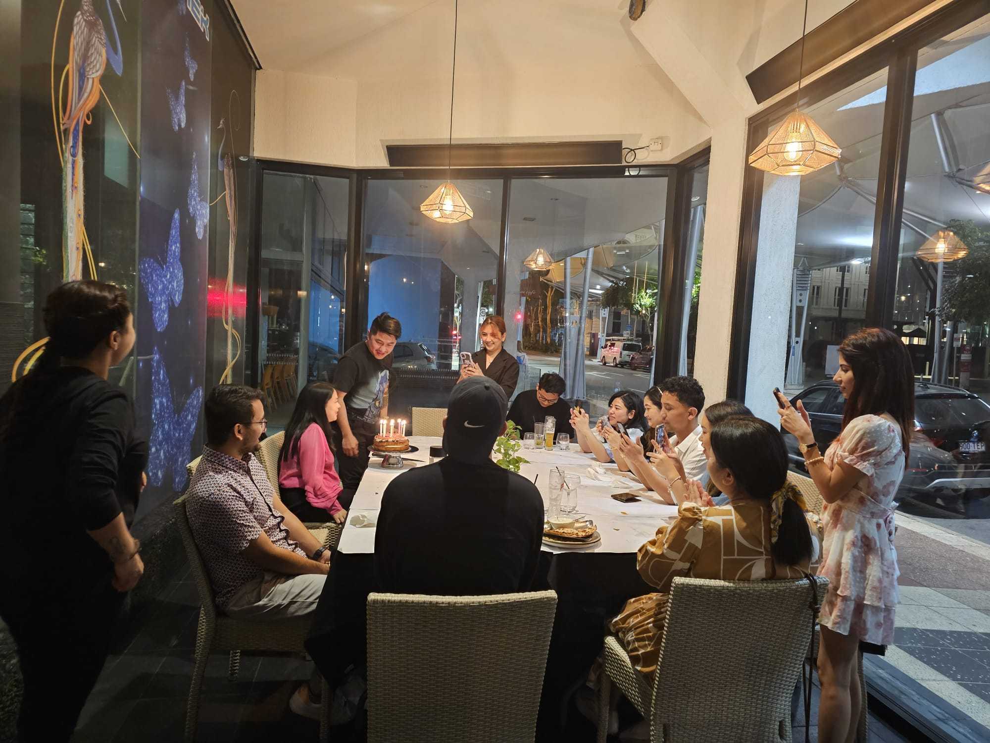 Guests celebrating around a birthday cake at a window table
